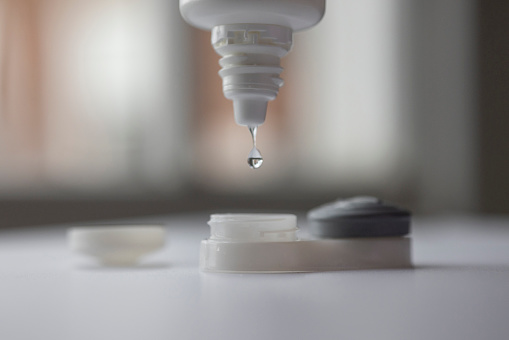 Close up of a saline dropping out of a bottle into a contact lens case.