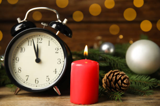 istock Alarm clock, burning candles and Christmas decor on wooden table, bokeh effect 1407314411