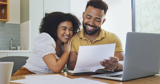 Couple celebrating financial freedom, using laptop, banking reports or statements to calculate budget, savings and finance. Happy debt free girlfriend and boyfriend with mortgage home loan approval stock photo