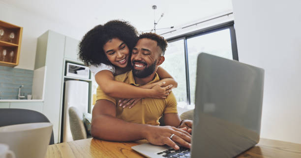 istock Woman hugging her working husband from behind while he sits with laptop at home. Afro man working remotely or freelance job using wifi and enjoying the flexible time with a his loving supporting wife 1407315633