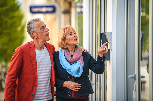 Waist up front view of a cute caucasian senior couple walking outdoors. They are looking at the windows of the stores.