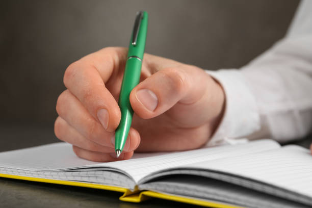 istock Man writing with pen in notebook at grey table, closeup of hand 1407316286