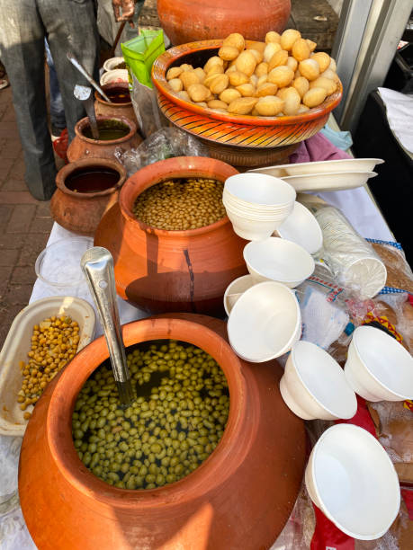 Image of Indian street food stall, pani puri snacks served with flavoured water (mint / masala) and chickpeas, matki (earthenware pot), elevated view, focus on foreground Stock photo showing elevated view of street food stall with pani puri snacks being served with chickpeas in flavoured water (mint / masala) from a matki (earthenware pot). panipuri stock pictures, royalty-free photos & images