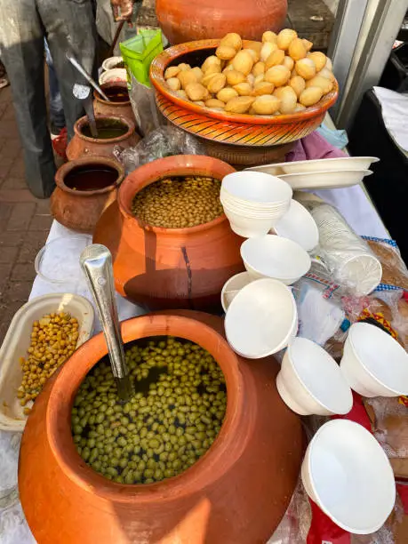Stock photo showing elevated view of street food stall with pani puri snacks being served with chickpeas in flavoured water (mint / masala) from a matki (earthenware pot).