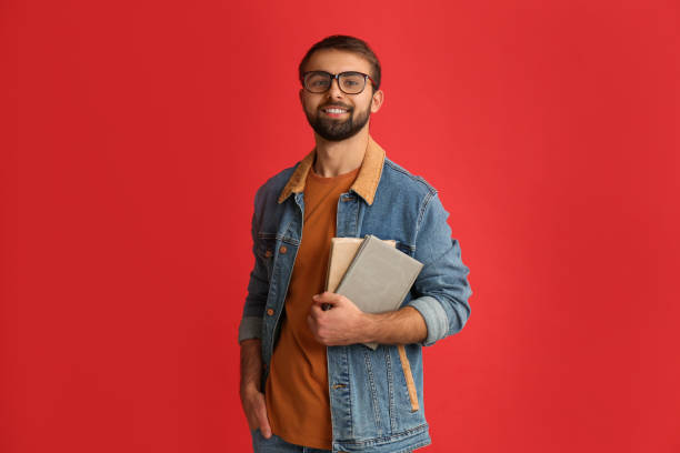 赤い背景の本を持つ幸せな学生 - scholarship holder ストックフォトと画像