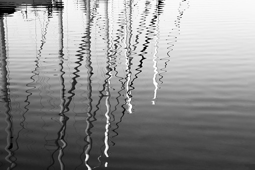 Reflection of many yacht masts in calm sea water. Beautiful sea background black and white photo