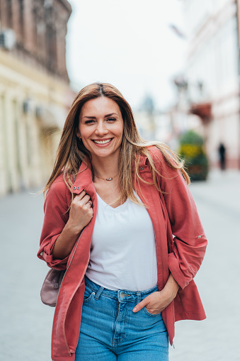 Portrait of cheerful woman in the city. Beautiful young woman enjoying sunny day on the city street. Happy woman smiling and looking at camera