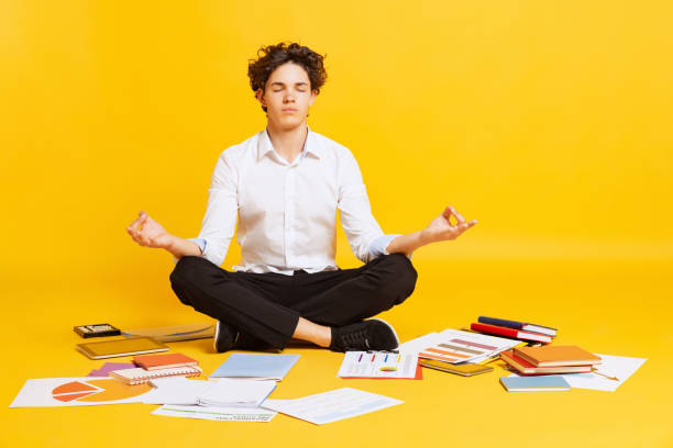istock Young boy, student in white business style clothes sitting on floor and doing homework isolated over yellow background. Back to school, university 1407319528