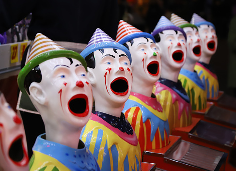 A row of colourful toy clowns with open mouths, an attraction at a fair, close up