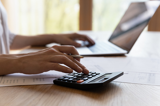 Close up cropped young woman calculating household expenditures, managing monthly budget, involved in financial accounting using computer applications, paying for services online, investment concept.