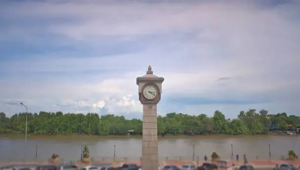 Chachoengsao , Thailand - 7 July 2022: Take in the view on the Bang Pakong River Promenade, where the clock tower contrasts with the blue sky and soft clouds.clock tower riverside street in the natural city of asia,city background