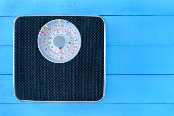 Mechanical weight scale, body mass control concept : Bathroom scale on pale blue wood background. Analog scale operated with spring that pressure is calibrated to translate tension into a mass readout.
