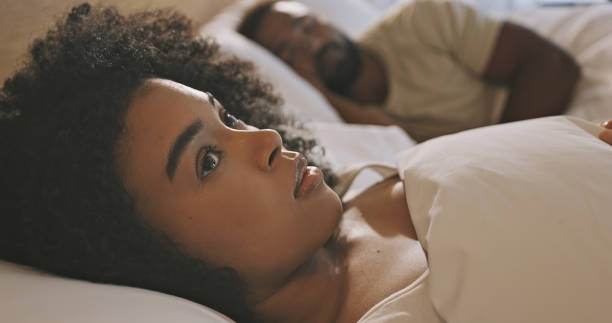 обеспокоенная чернокожая женщина, лежащая в постели с бессонницей, выглядит тревожной и обеспокоенной, имеющей измену и проблемы в отношен - displeased women irritation couple стоковые фото и изображения