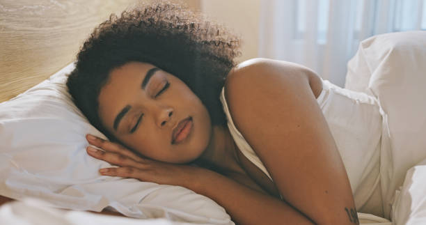 mulher com afro dormindo sozinha em sua cama quente em casa durante a manhã. descansando e sonhando em um quarto confortável sozinho. corpo e mente relaxados se atualizando sobre o sono rem para sistema imunológico saudável - rem - fotografias e filmes do acervo