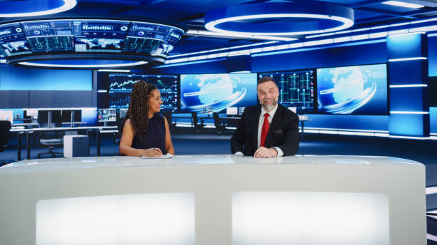 istock TV Live News Program: Two Professional Presenters Reporting On the Events. Television Cable Channel Newsroom Studio: Male and Female Anchors Talk. Mock-up Broadcasting Network Concept. Wide Shot 1407334002
