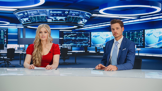 TV Live News Program: Two Presenters Reporting, Discuss Daily Events, Business, Economy, Science, Entertainment. Television Cable Channel Diverse Anchors Talk. Newsroom Studio Concept