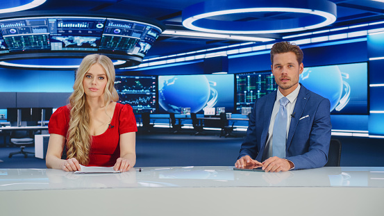 TV Live News Program: Two Presenters Reporting, Discuss Daily Events, Business, Economy, Science, Entertainment. Television Cable Channel Diverse Anchors Talk. Newsroom Studio Concept