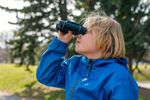 enfant regardant à travers des jumelles dans le parc. garçon explorant la faune. observation des oiseaux et aventure - discovery binoculars boy scout searching photos et images de collection