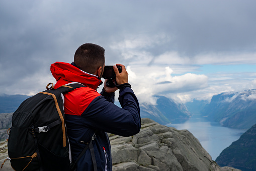 Young male tourist photographing the Lysefjord from Preikestolen