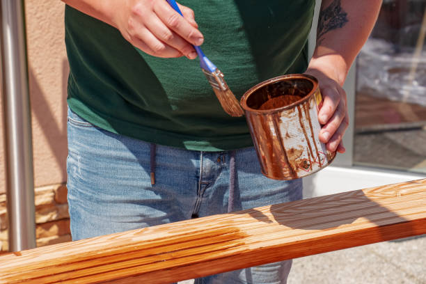 Close up male hands holding a brush and painting a rough varnish on the background of the surface of a wooden board stock photo