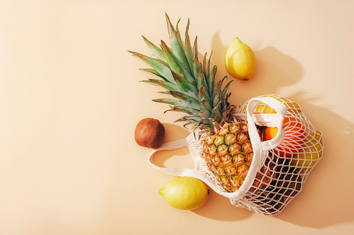 Pineapple, lemons, oranges and kiwi fruits in a string bag. Zero waste concept, healthy food. Top view, flat lay.