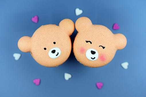 Cute macarons in a shape of bears, blue background, small hearts around. Love concept