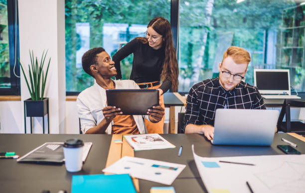 startups alegres desfrutando de cooperação em espaço confortável de coworking para usar internet sem fio de alta velocidade em laptop digital e touch pad para informações de pesquisa, grupo de jovens inteligentes bem-sucedidos - computer team young adult smart casual - fotografias e filmes do acervo