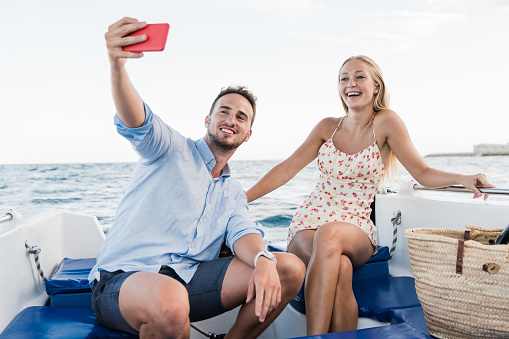 Happy young couple having fun on sailing boat during luxury summer vacations - Millenials taking selfie at the beach - Focus on girl face