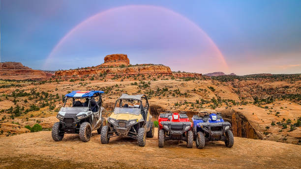 4 wheeler ATV and side by side UTV lined up on sandstone with a beautiful butte and rainbow in the background. RZR Along the off road  Jeep and 4 wheeler trails near Moab, Utah.