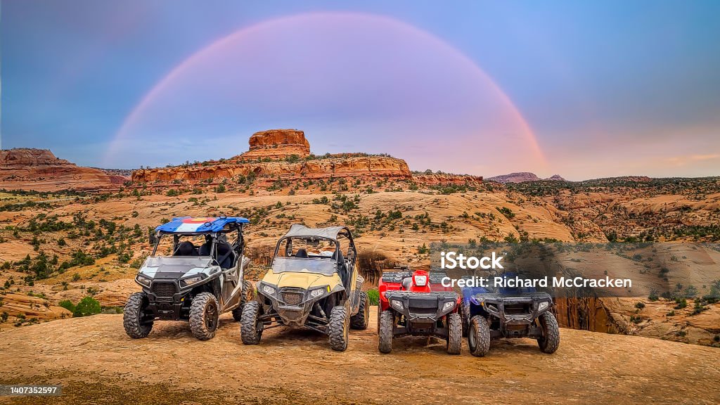 4 wheeler ATV and side by side UTV lined up on sandstone with a beautiful butte and rainbow in the background. RZR Along the off road  Jeep and 4 wheeler trails near Moab, Utah. Off-Road Vehicle Stock Photo