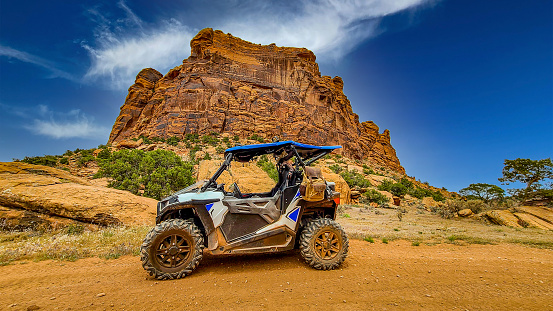 4 wheeler ATV and side by side UTV lined up on sandstone with a beautiful butte and rainbow in the background. RZR Along the Onion Creek off road Jeep and 4 wheeler trails near Moab, Utah.