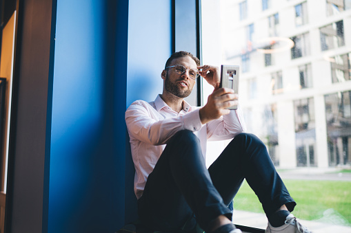 Handsome Caucasian man in eyeglasses installing network application for web socialising in online mode, millennial male blogger reading received smartphone message during content chatting and texting
