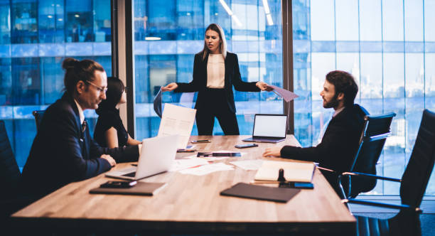 istock Puzzled female director in elegant suit communicating with employees during working process in conference room standing near meeting table with modern technology, laptop with mock up for website 1407354635