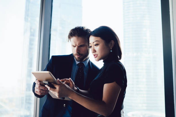 Diverse male and female partners checking mail on touch pad during working time in company office, multicultural entrepreneurs using technology for online banking operation connected to 4g wireless