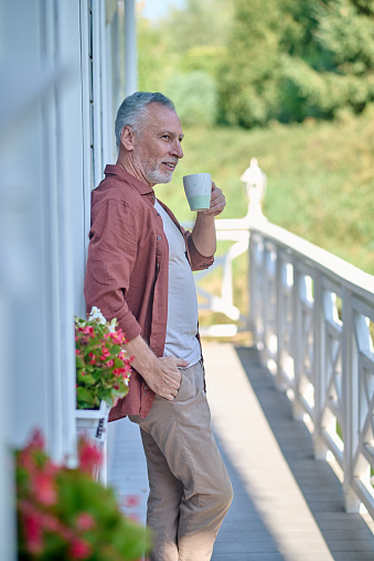 Weekend. Gray-haired man having coffee on his house terrace