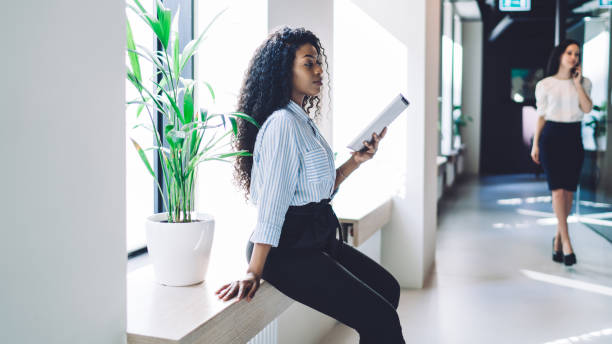 istock Attentive ethnic businesswoman browsing tablet while rest on window sill 1407355860