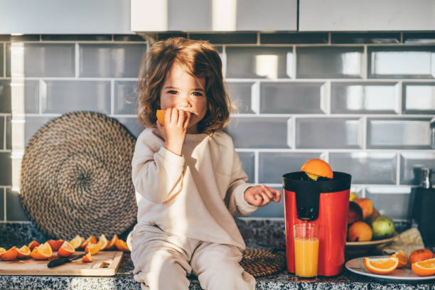 little baby girl makes freshly orange juice. - freshly squeezed orange juice imagens e fotografias de stock