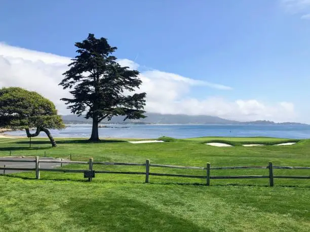 Photo of A beautiful view from a public viewing area of the green of the 18th hole at pebble beach golf course with the ocean in the background, on a beautiful sunny spring day.