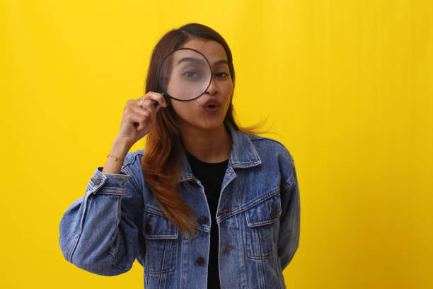 istock Funny asian woman standing while looking through magnifying glass. Investigation concept 1407360207