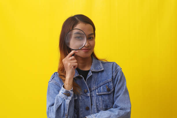 istock Smiling asian woman standing while looking through magnifying glass. Isolated on yellow background 1407360364