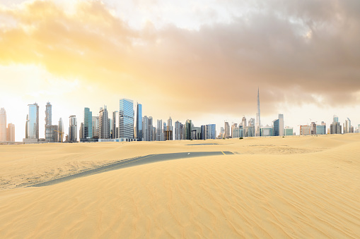 Stunning view of a road covered by sand dunes with the Dubai Skyline in the distance. Dubai, United Arab Emirates.