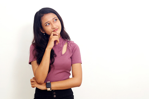 Photo of thinking young asian woman isolated over white background looking aside.