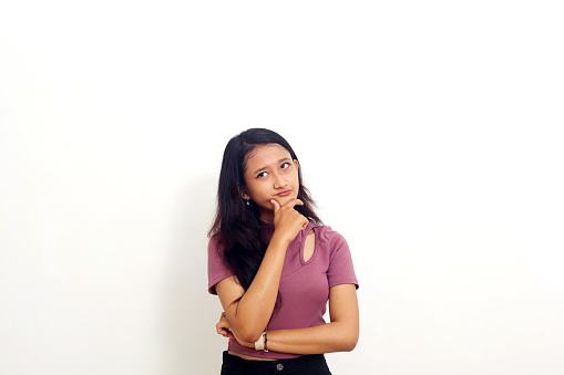 Photo of thinking young asian woman isolated over white background looking aside.