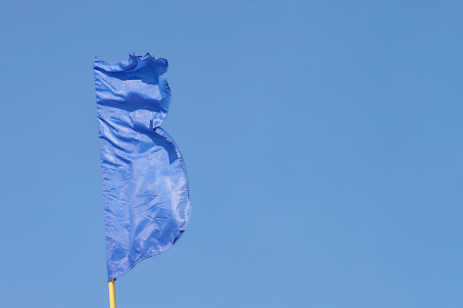 a blue flag waving in the wind against a cloudless blue sky