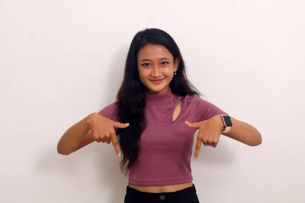 istock Asian girl smiling stand makes gesture two fingers pointing down presenting and looking to camera 1407366170