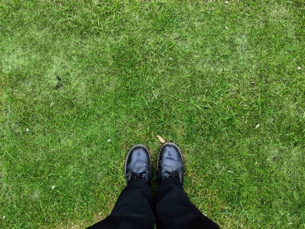 istock Two black shoes and legs on a grass surface - top view concept. 1407368895