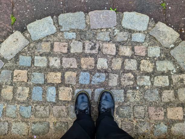 istock Two black shoes and legs on a cobblestone surface - top view concept. 1407368920