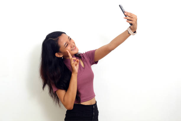 istock Cheerful young asian girl standing while doing selfie. Isolated on white background 1407369074