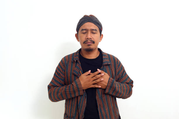 Asian man in java traditional costume standing while holding his chest. He is feels relieved