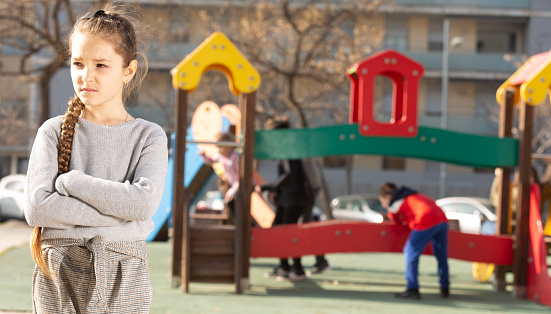 Portrait of offended girl not playing with friends after quarrel on playground